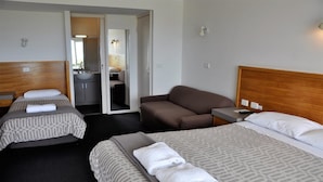 Ein Hotelzimmer mit zwei Betten, einem Schlafsofa, einem kleinen Tisch und einem durch eine offene Tür einsehbaren Badezimmer.
