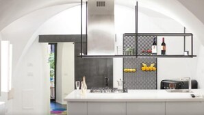 Una cocina moderna con encimera blanca, protector contra salpicaduras de malla negra y una lámpara colgante.