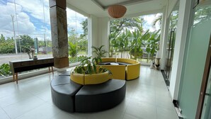 Un vestíbulo moderno con una zona de estar curva en negro y amarillo, ventanas amplias y plantas de interior.