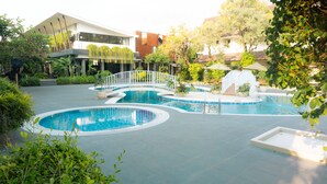 Un área de piscina moderna con varias piscinas circulares, rodeada de abundante vegetación y una cerca blanca.