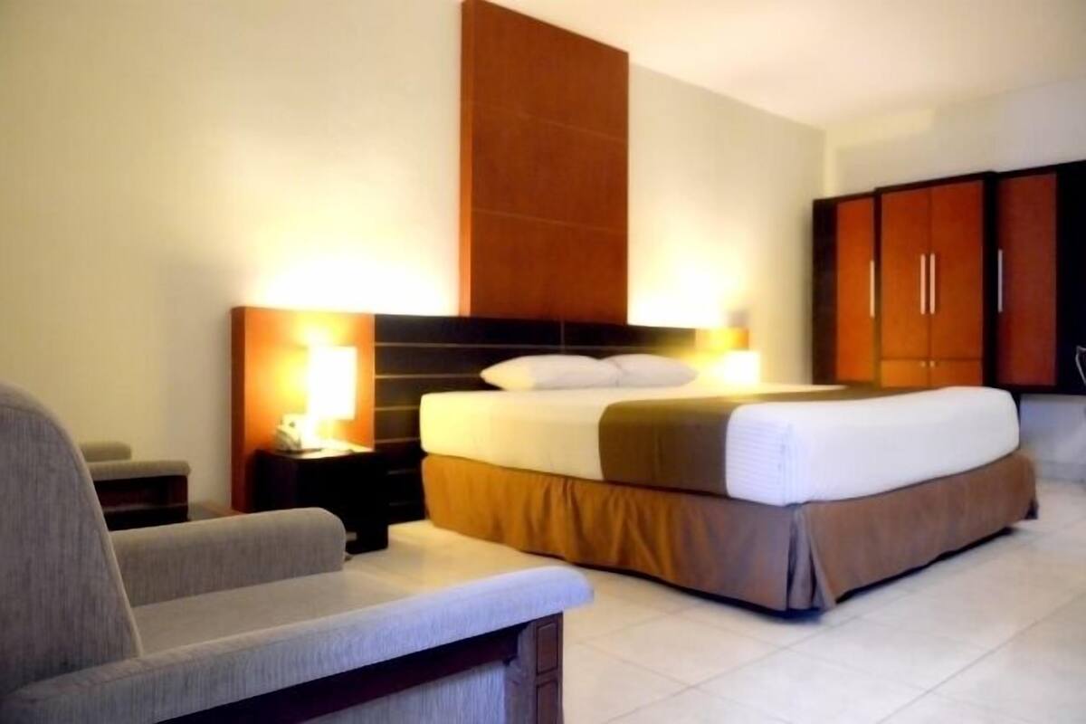 Une chambre d’hôtel comprenant un lit, une table de chevet, une lampe et une armoire.