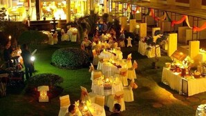 Evento al aire libre con mesas redondas dispuestas para comer, rodeado de asistentes.