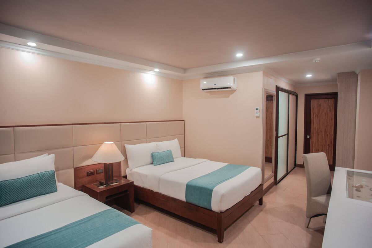 Una habitación de hotel con dos camas, un escritorio y un aire acondicionado.