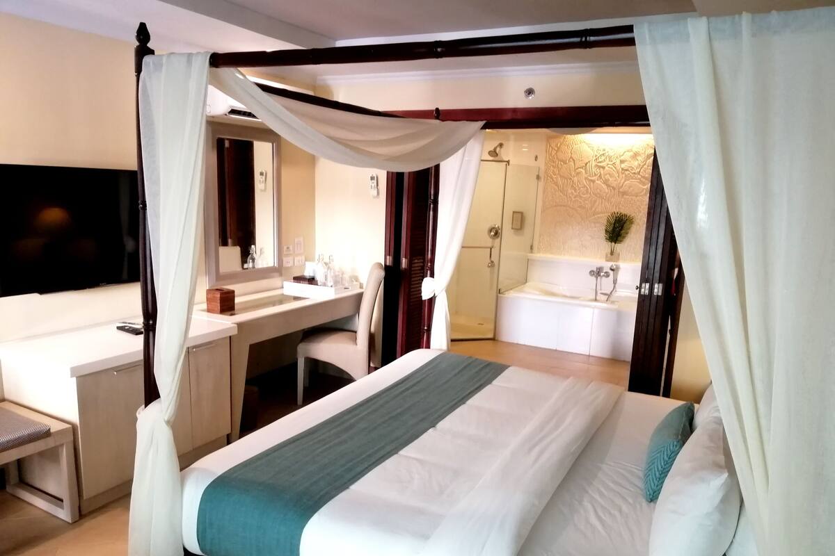 Habitación de hotel con cama, escritorio, televisión y baño con bañera y ducha.