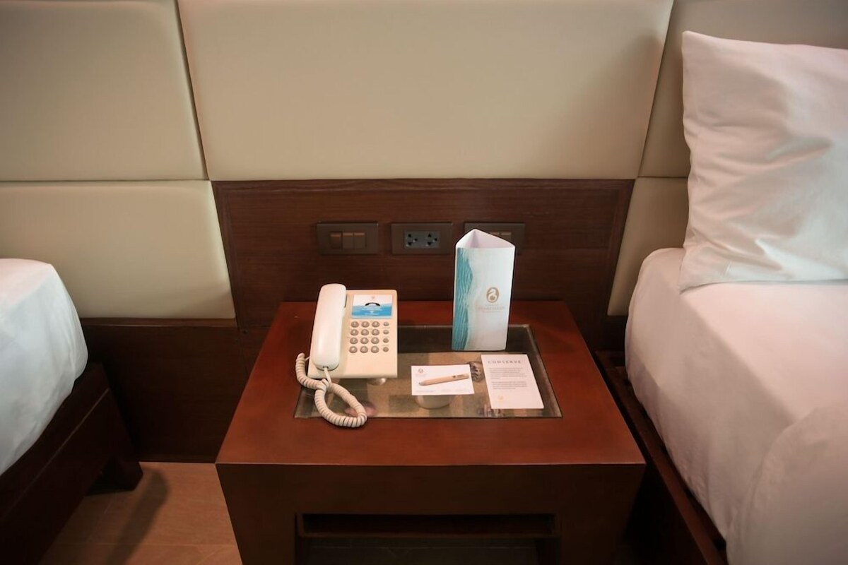 Een hotelkamer met een nachtkastje waarop een telefoon, een doos zakdoekjes en een klein boekje staan.