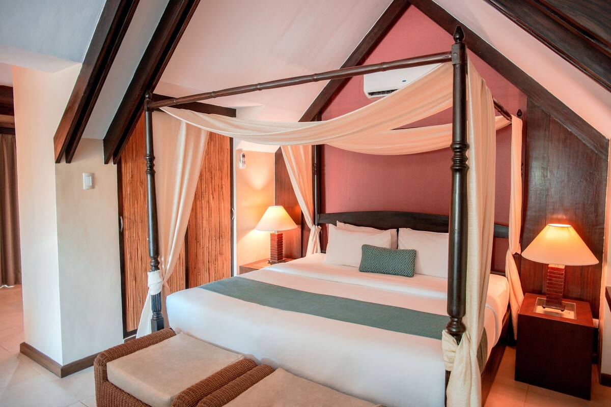 Una cama con dosel y cortinas, una mesita de noche con lámpara y un cabecero de madera.