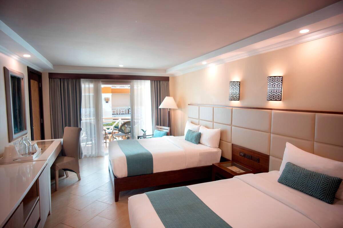 Una habitación de hotel con dos camas, un escritorio y vistas a un balcón.