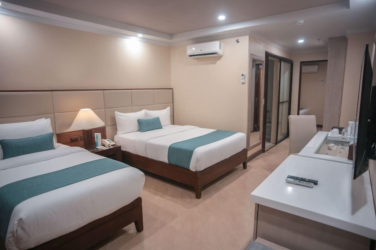 A hotel room with two beds, a desk, a chair, and a TV.