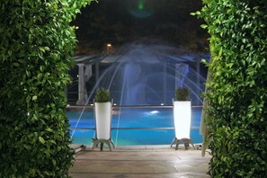 A pool area with a water feature, surrounded by greenery and a covered structure. - Villa Masseria Marini (San Giuseppe Vesuviano)