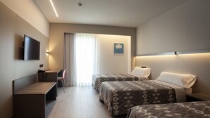 Habitación de hotel con dos camas, un escritorio, una silla, un televisor y una ventana con cortinas.