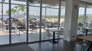 Un comedor moderno con amplios ventanales, asientos exteriores y vista a un estacionamiento.