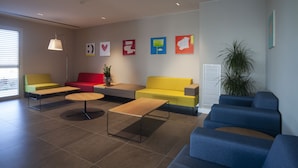 Un área de espera moderna con un sofá amarillo, un sofá rojo, un sofá azul y una mesa de centro de madera.