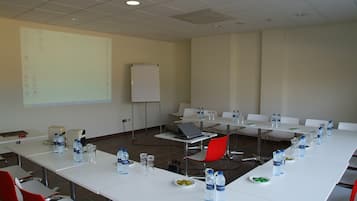 A conference room with white tables, red chairs, water bottles, and a laptop.