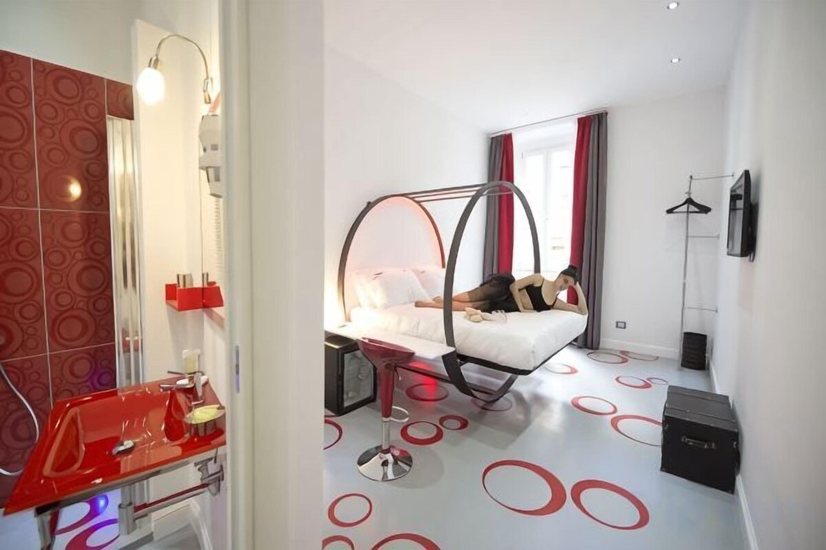 Une chambre d’hôtel moderne avec un lit suspendu, un lavabo rouge et un miroir.