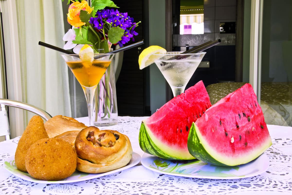Una mesa con una fuente de cruasanes, un vaso de té helado, un martini y una rebanada de sandía.