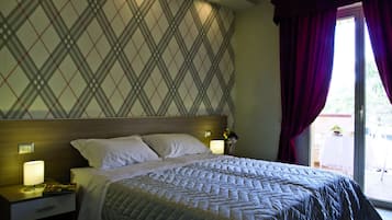 Habitación de hotel con cama, mesitas de noche, lámpara y vistas al exterior.