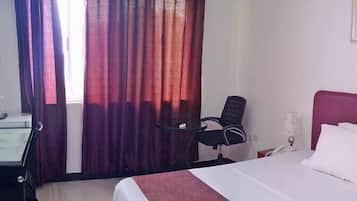 A hotel room with a bed, a desk, a chair, and a TV.
