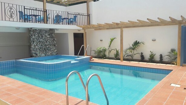 A swimming pool with a hot tub, surrounded by a patio area with chairs and plants. - Lane Residence (Accra)