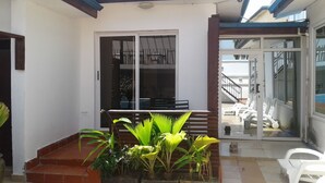 A covered patio area with a table and chairs, a staircase, and potted plants. - Lane Residence (Accra)