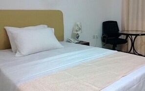 Una habitación de hotel con una cama, una mesita de noche con lámpara, una silla y una pequeña mesa.