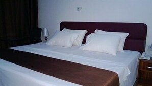 A neatly made bed with white bedding and a brown throw, a bedside lamp, and a wooden nightstand with a phone. - Lane Residence (Accra)
