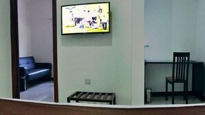 A room with a television mounted on the wall, a black leather sofa, a wooden bench, and a desk with a chair. - Lane Residence (Accra)