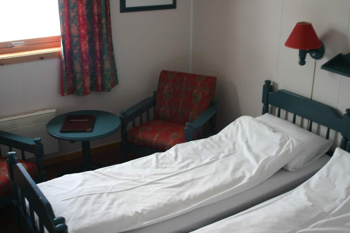 A small room with two single beds, a chair, a small table, and a lamp.