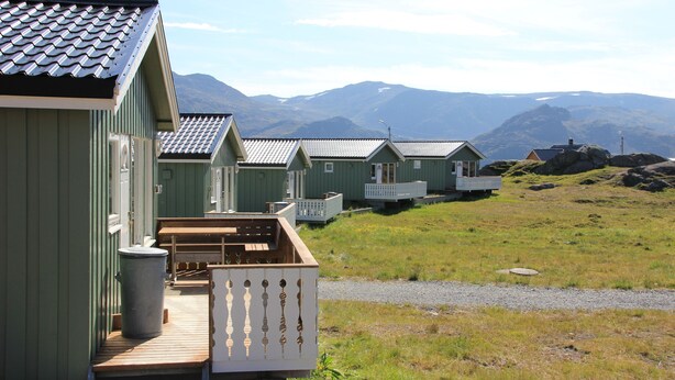 A row of green cabins with wooden decks and a gravel path leading to them. - Nordkapp Camping (Nordkapp)