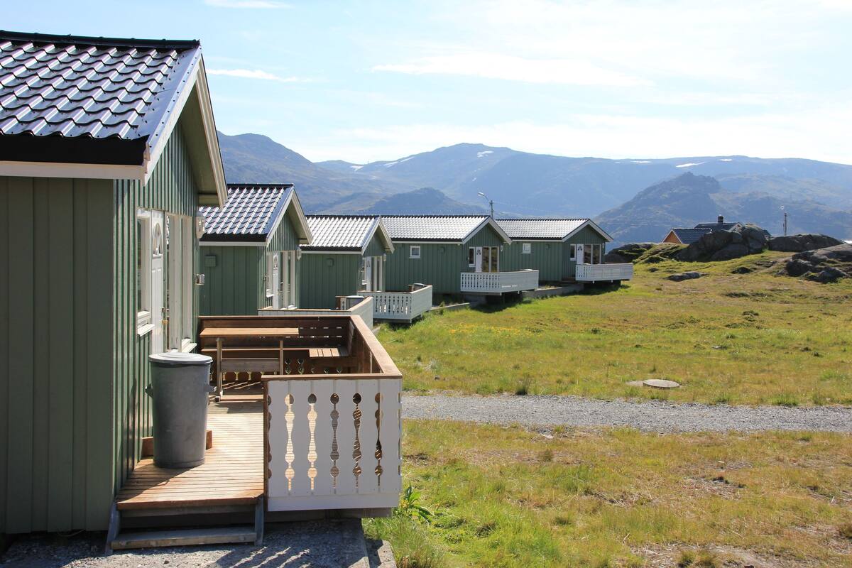 A row of green cabins with wooden decks and a gravel path leading to them.