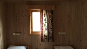 A room with two wooden beds, a small table, and a window with curtains. - Nordkapp Camping (Nordkapp)