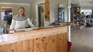 A wooden reception desk with a sign indicating payment in Euros. Behind the desk, there are shelves with various items, including magnets and postcards. - Nordkapp Camping (Nordkapp)