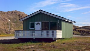 A small, single-story building with a green exterior and a white front door. It has a balcony with a white railing and a small porch area. - Nordkapp Camping (Nordkapp)