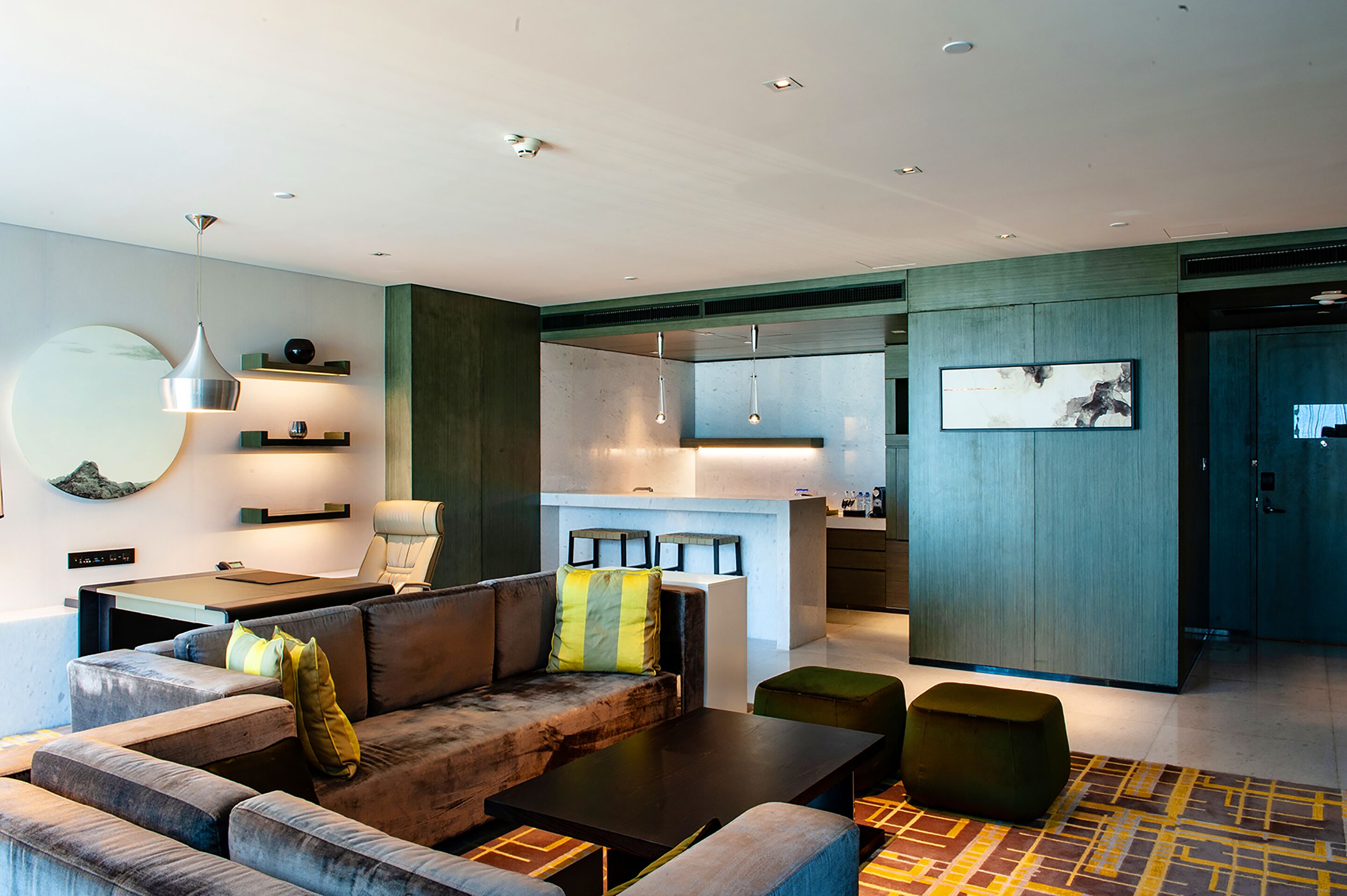 A modern living room with a sofa, coffee table, and ottoman, a dining area with a table and chairs, and a kitchen area with a counter and cabinets.