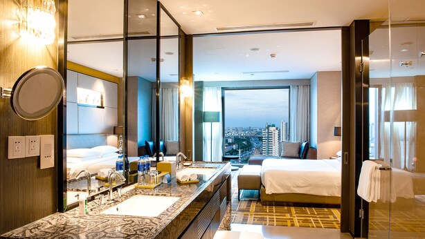A hotel room with a large mirror, a marble bathroom vanity, a bed, a sofa, and a view of the city. - Hyatt Regency Tianjin East (Tianjin)