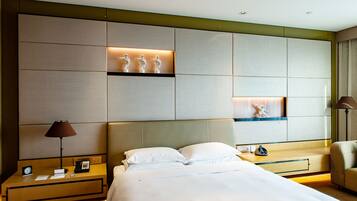 A hotel room with a large bed, two bedside tables, a nightstand, a desk, and a chair. There are wall-mounted shelves with decorative items.