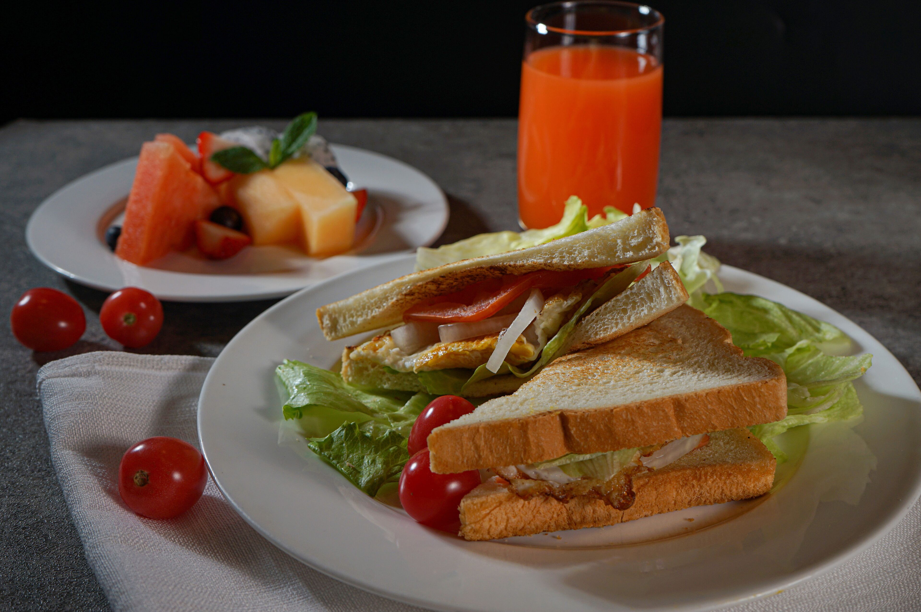 A plate with a sandwich, lettuce, and cherry tomatoes.