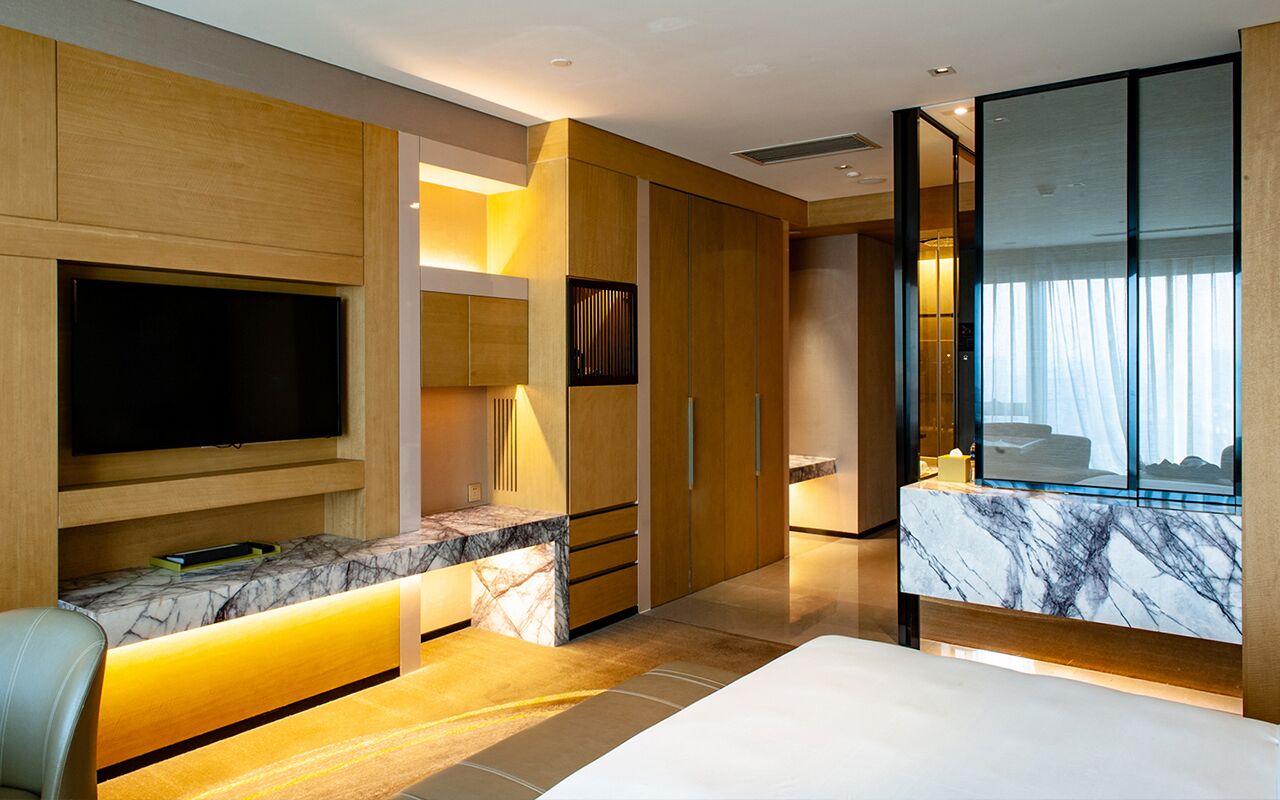 A modern hotel room with a large flat-screen TV, a marble bathroom vanity, a bed with a view, and a sliding door closet.