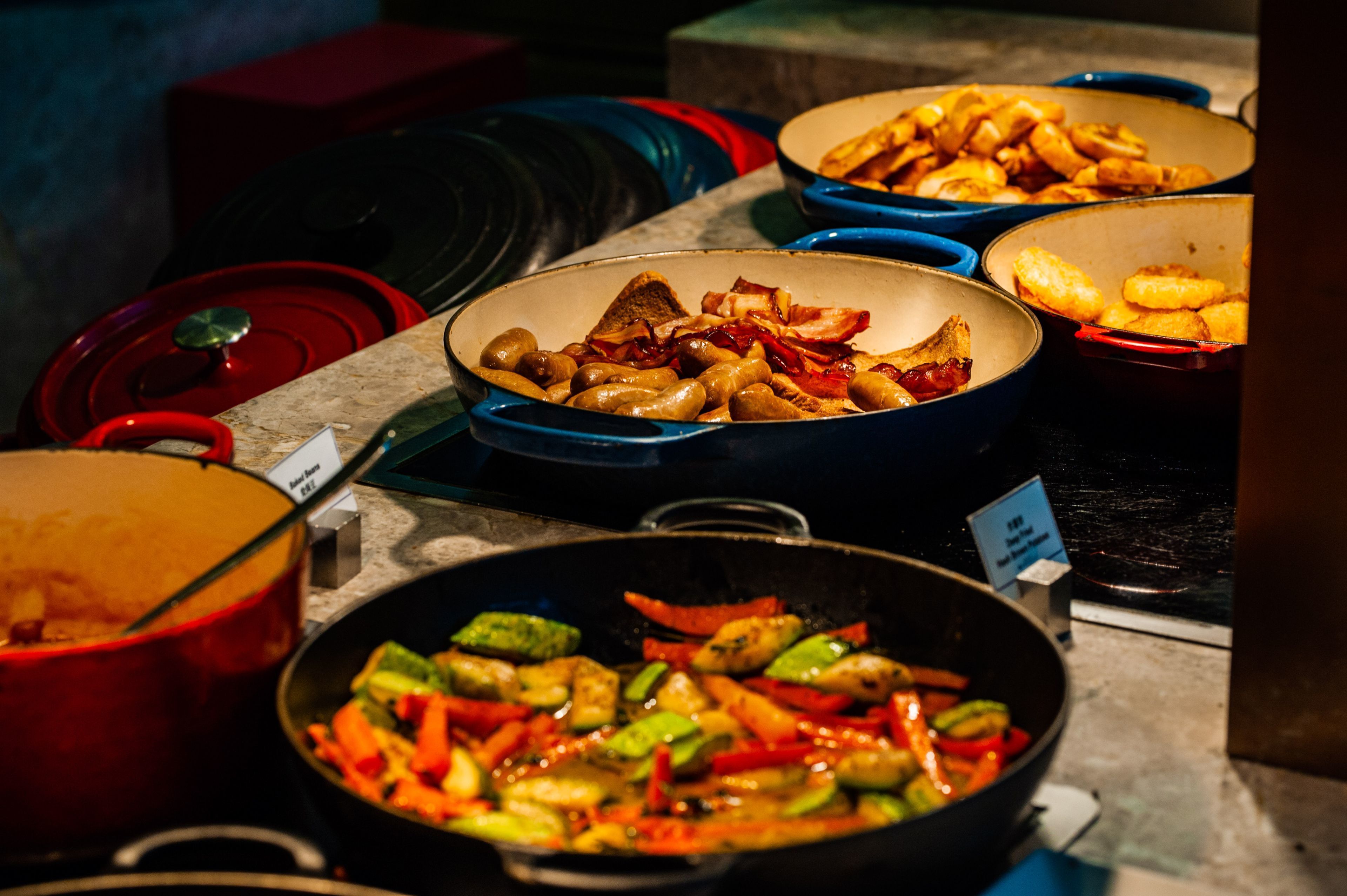 Un bufé con diversos platos, incluyendo pollo frito, verduras y otros alimentos preparados.