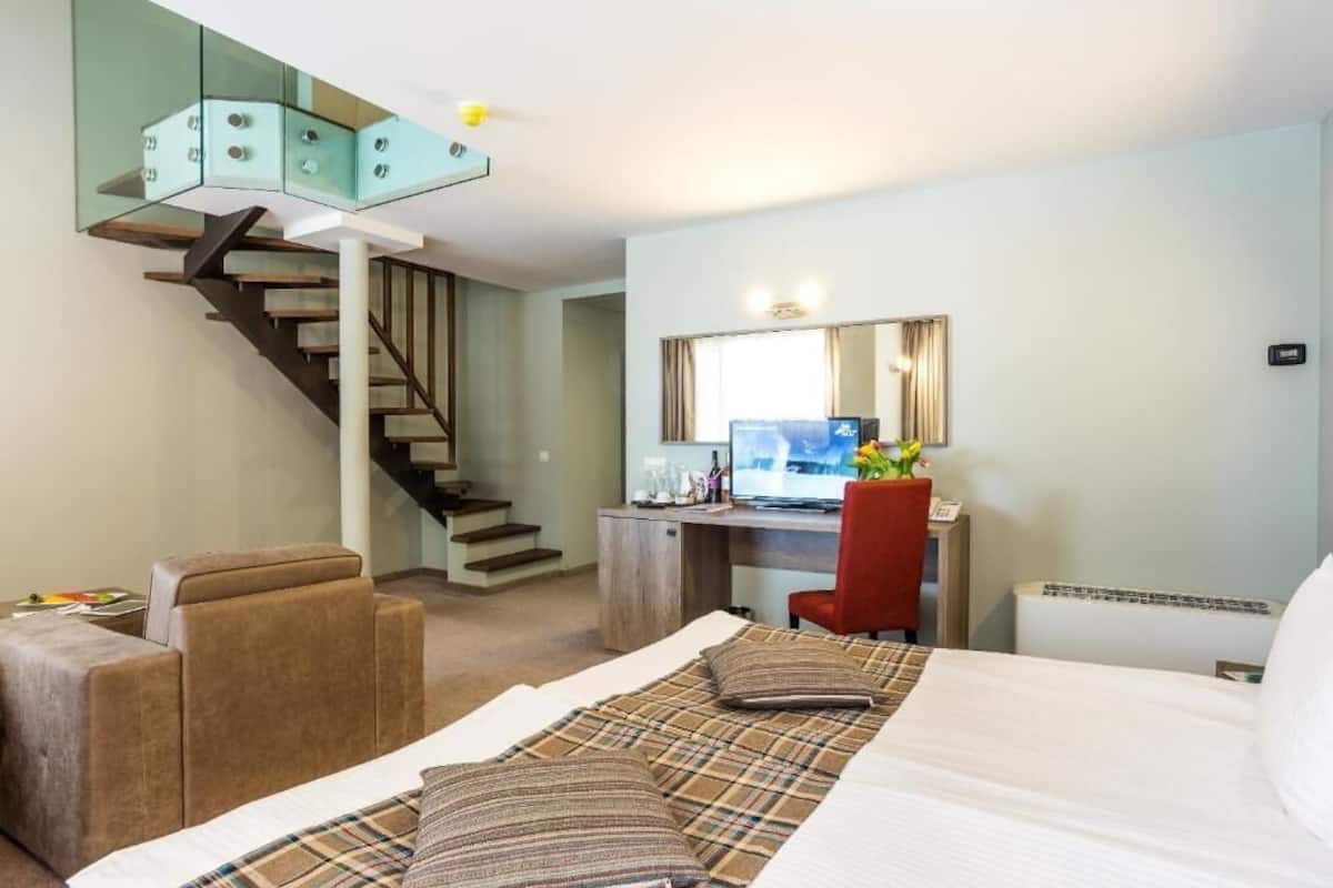 Ein Hotelzimmer mit Bett, Schreibtisch, Sessel, Sofa, Treppe und Spiegel.