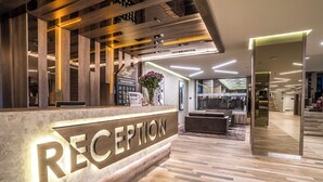 Ett entréområde med en receptionsdisk i trä, en skylt som visar var receptionen finns och en trappa som leder till andra delar av byggnaden.