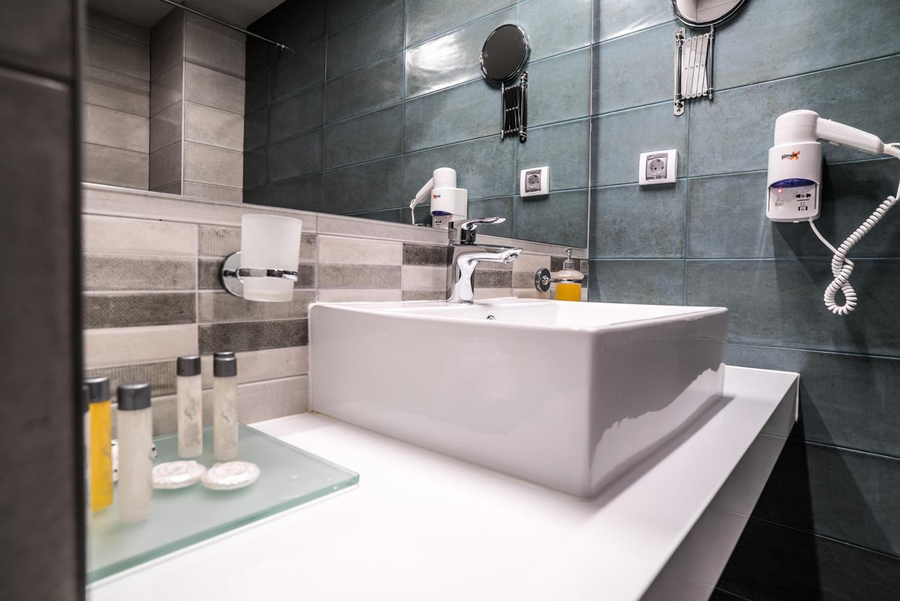 Ein modernes Badezimmer mit einem großem rechteckigen Waschbecken, einem Spiegel, einem Föhn und Toilettenartikeln auf der Ablagefläche.