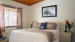 A neatly arranged bedroom with a large bed, two bedside tables, a chair, and a window with curtains. - Redwood Suites (Ferndale)