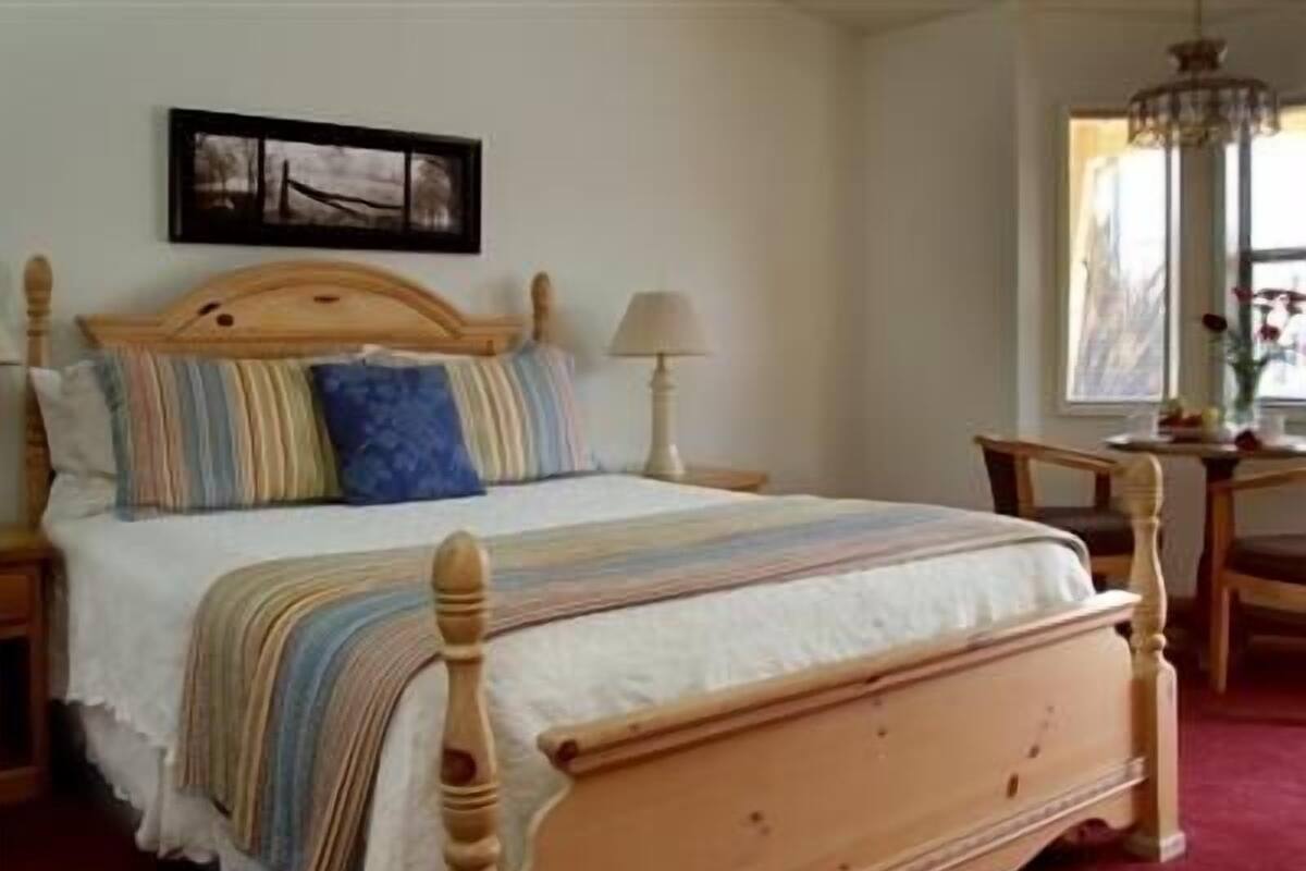 A wooden four-poster bed with a white bedspread and striped pillows, a nightstand with a lamp, and a framed picture on the wall.