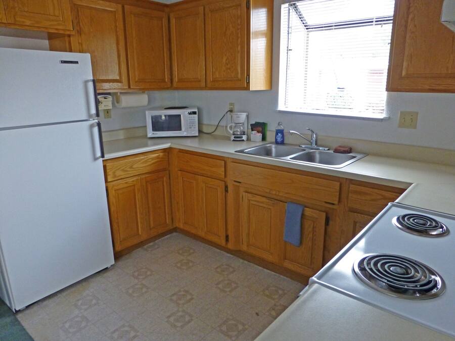 A kitchen with wooden cabinets, a white refrigerator, a microwave, a sink, and a stove.