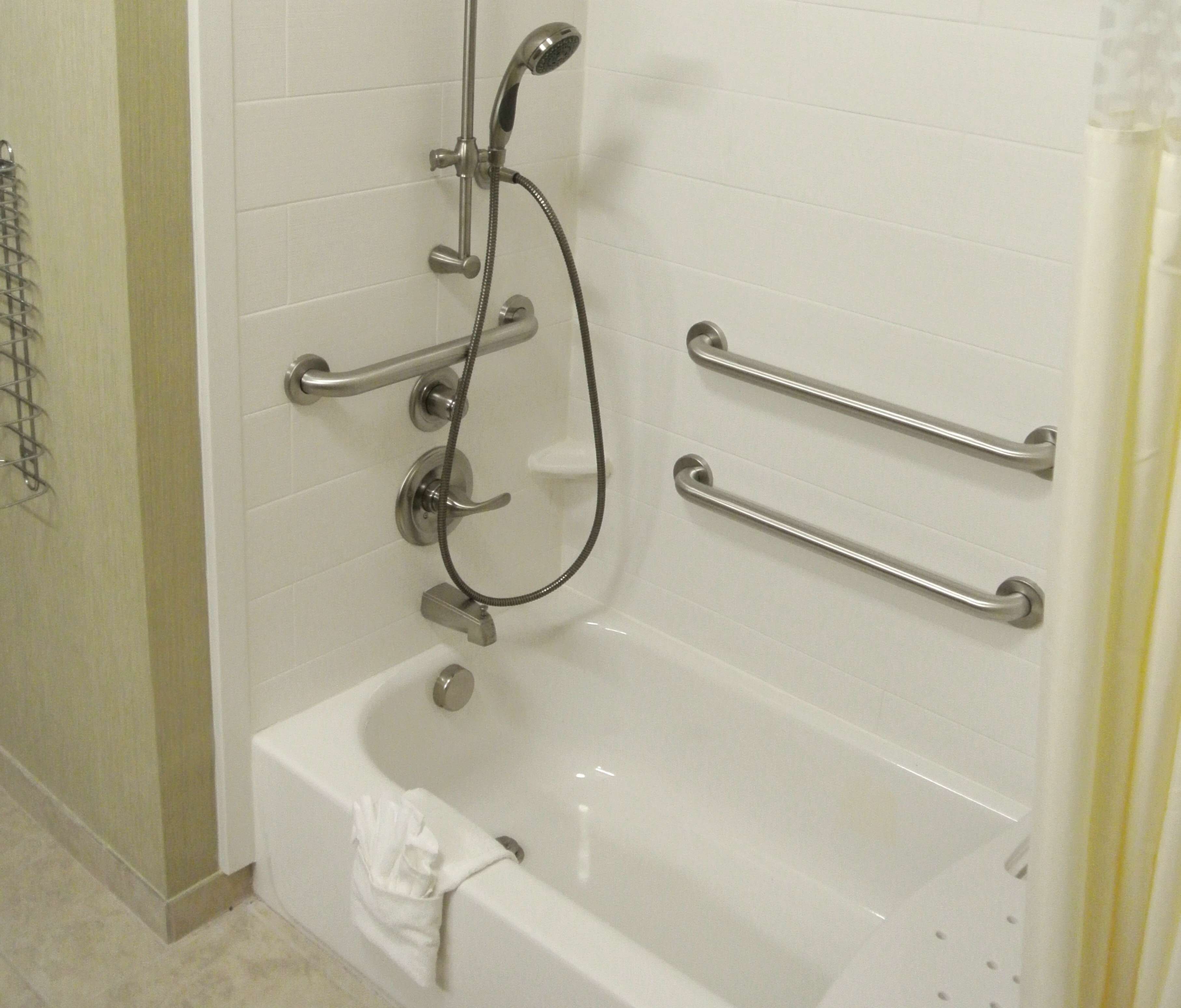 Ein Badezimmer mit einer weißen Badewanne, Haltegriffen und einer Duschbrause.