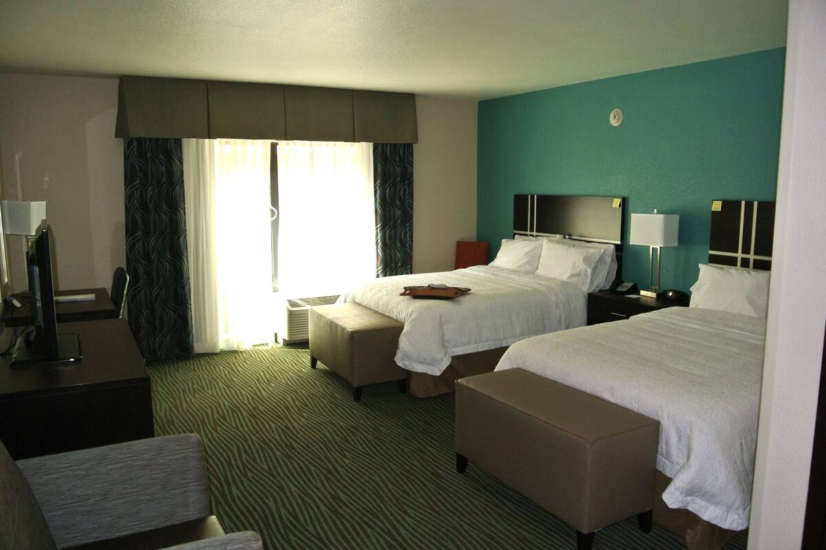 A hotel room with two beds, a desk, a chair, and a window with curtains.