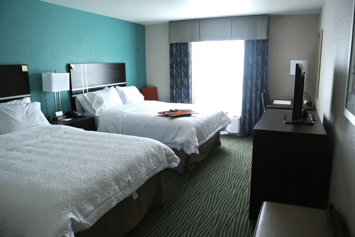 A hotel room with two beds, a desk, a TV, and a window with curtains.