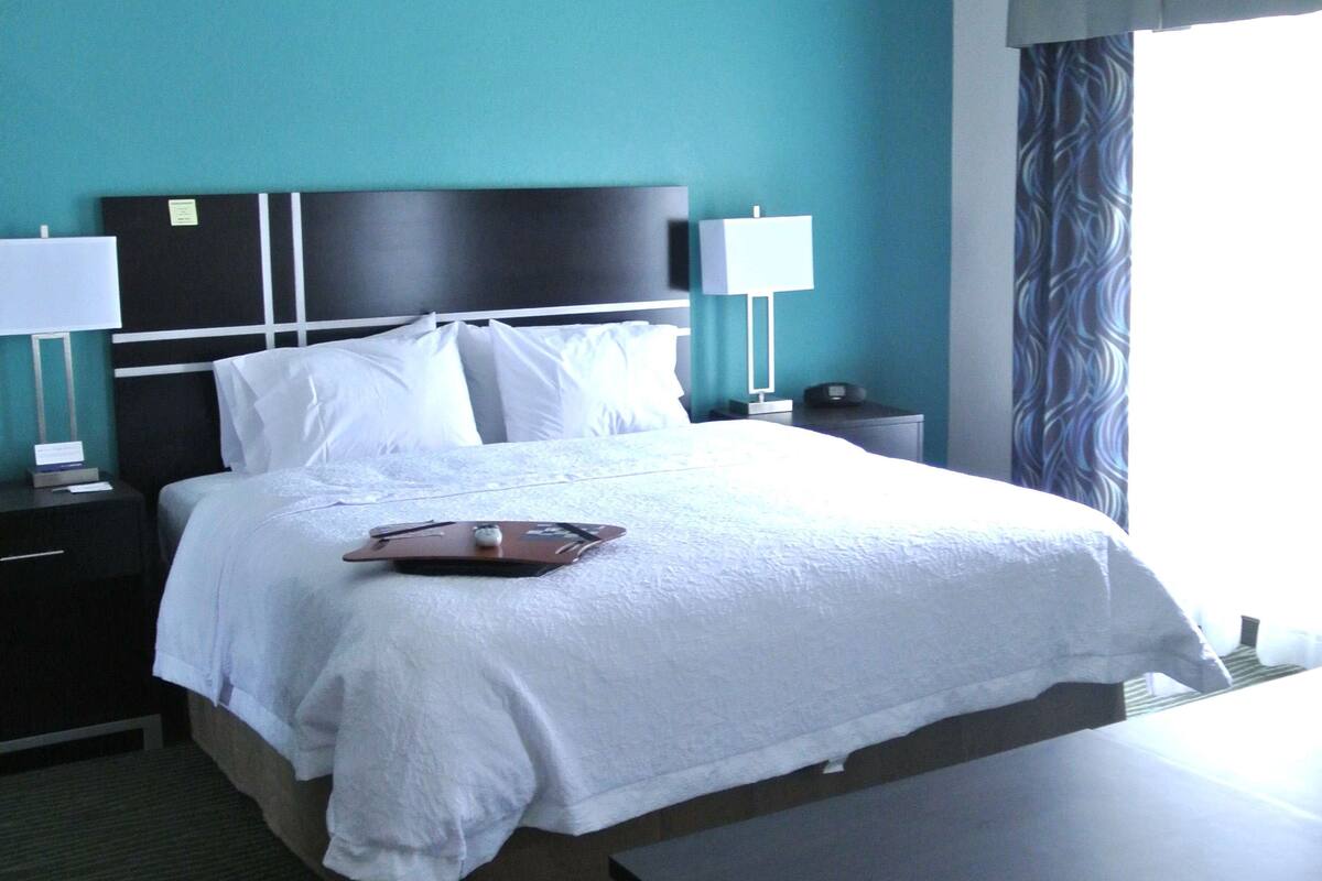 A hotel room with a large bed, two bedside tables, a desk, and a window with curtains.