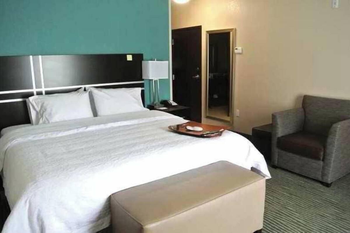 A hotel room with a bed, a bedside table, a chair, and a mirror.