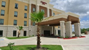 A Hampton Inn hotel with a stone facade, multiple windows, and a palm tree in the foreground. - Hampton Inn Carrizo Springs (Carrizo Springs)